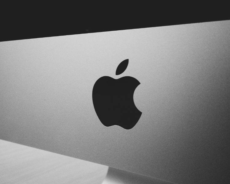 The official black Apple logo design is below a silver iMac's screen.