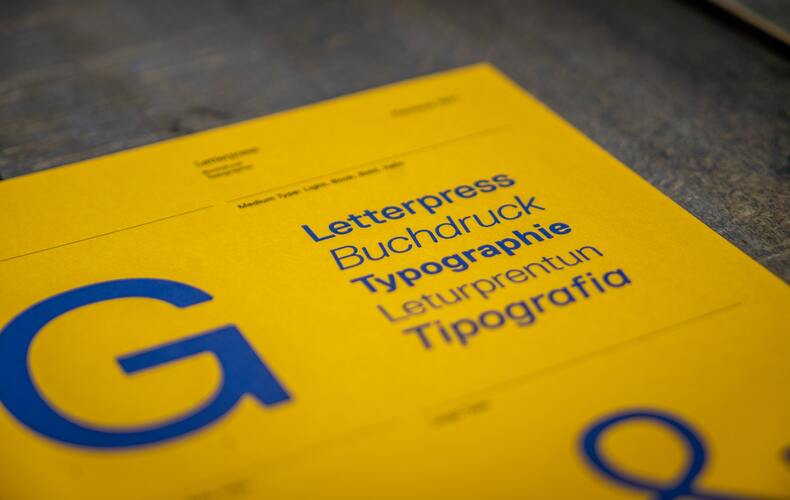 A yellow guidebook on a black, blurry background has a blue font showcasing different typographies. 