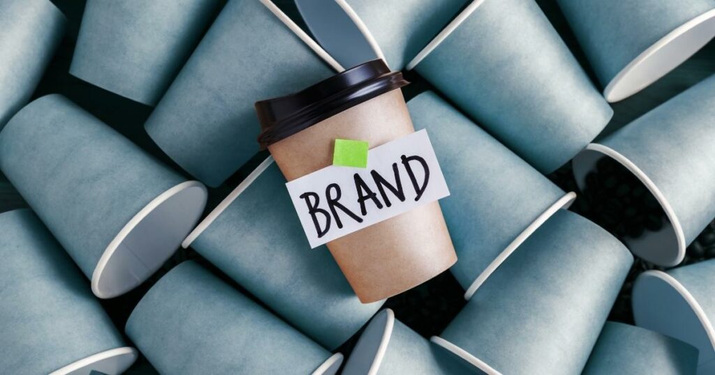 Brand written on a paper attached to a brown paper cup with a black lid using green tape.