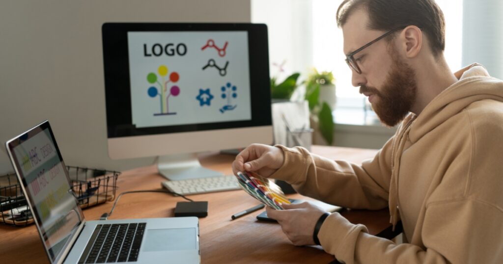 man choosing color scheme for his designing project in front of his monitor, laptop, and while sitting in front of his table