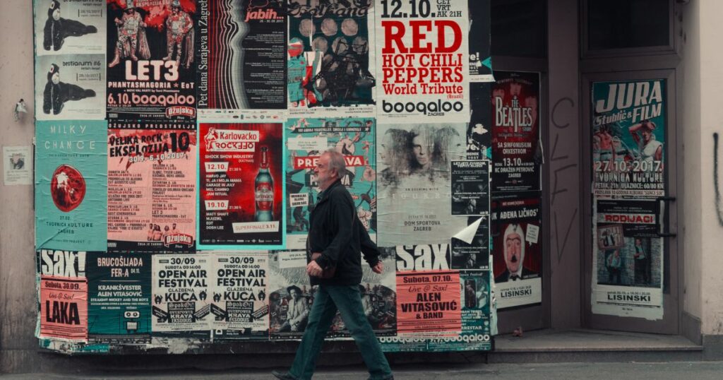 A man wearing jeans and a jacket walks by banners and posters on the side wall.