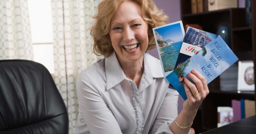 A smiling older woman is holding three different travel brochures.