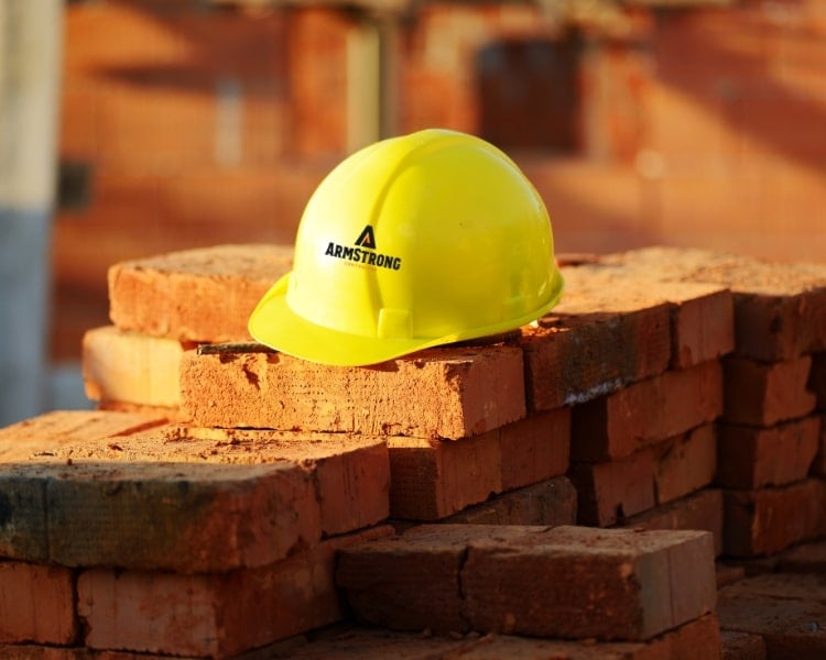 Over a pile of bricks is a yellow construction hard hat with a contractor company logo design.