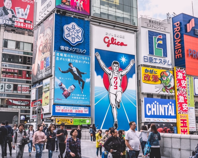 Multiple Japanese ads and billboards on buildings in a busy street full of people.