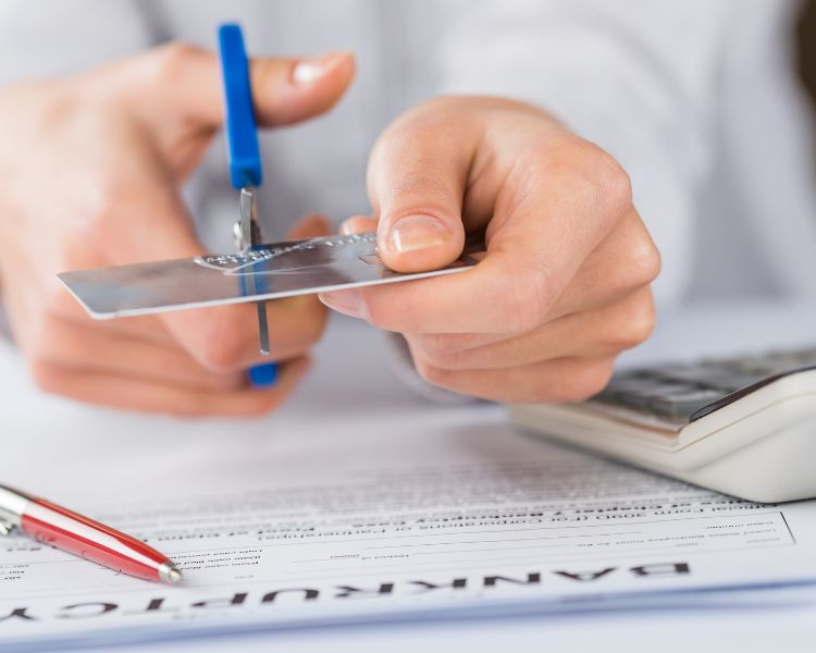 A photo of a person using a pair of scissors to cut a credit card in half.