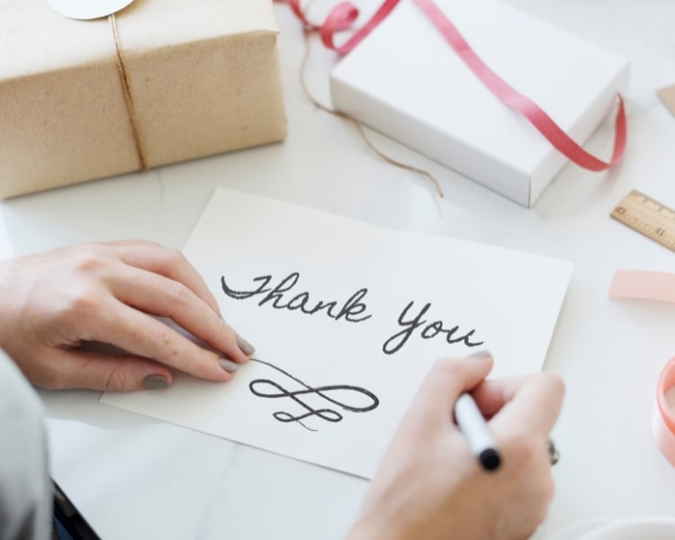 A person with colored fingernails wrote the word thank you on a white piece of paper.