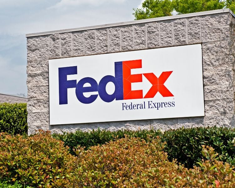 The logo design of the American brand FedEx signage on a white brick wall.
