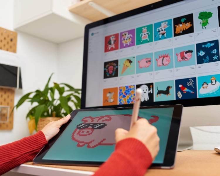 A person is creating an NFT art using a tablet and a stylus pen in front of a computer screen.