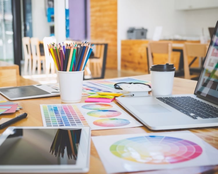 Different design tools both physical and digital over a wooden table.