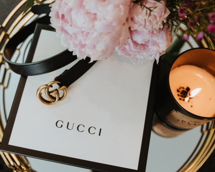 The logo of the Italian luxury fashion brand Gucci is printed on a gift box beside a lit candle in a glass.
