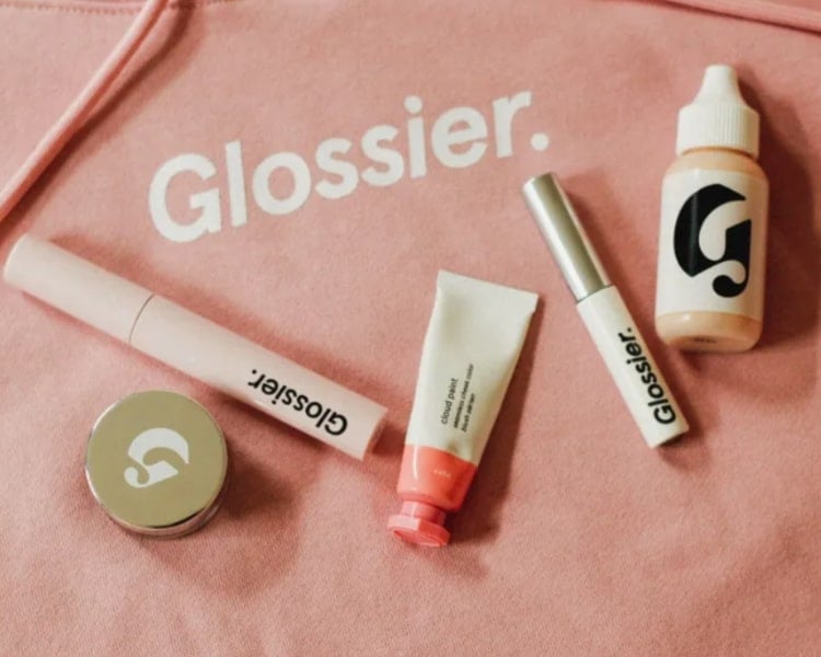 various glossier product placed in a pink glossier bag with a big wordmark logo printed in it