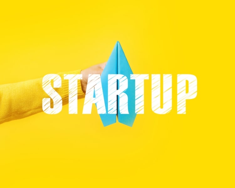 a picture of a startup with the word itself written on the center of the screen, with yellow background a a hand holding a blue paper plane