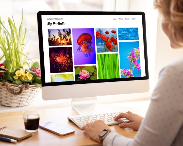 A woman is typing on a white keyboard while viewing a computer screen that displays various photos on a My Portfolio page of a website.