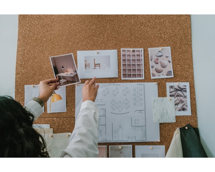 A woman wearing a white shirt is arranging mood board attached on the wall.