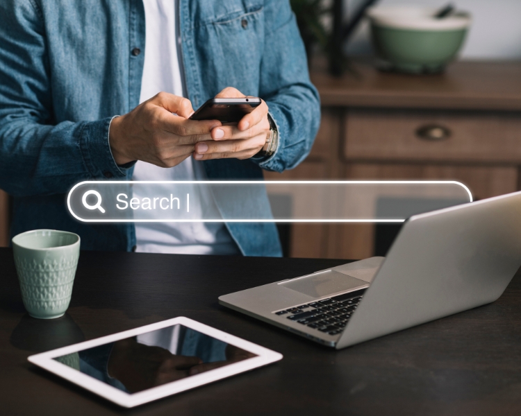 man using his phone in front of tablet and laptop with a search bar on the image right in front of the frame