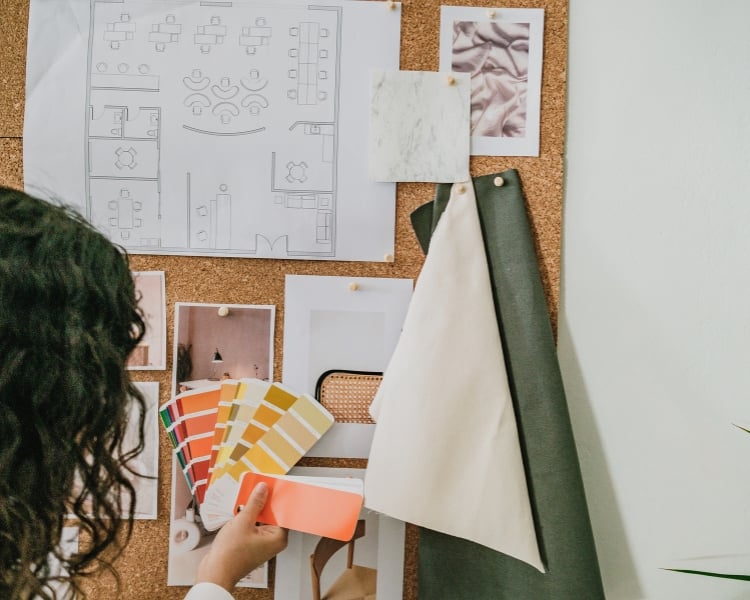 woman arranging the mood board attached on a wall and choosing a color scheme.