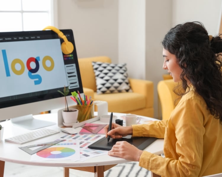 woman creating a logo using her pen and tablet with a monitor and editing software opened