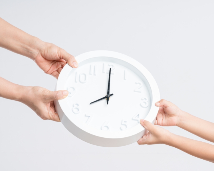 Two people holding a white clock side by side, with the clock hands pointing at 8 o'clock.