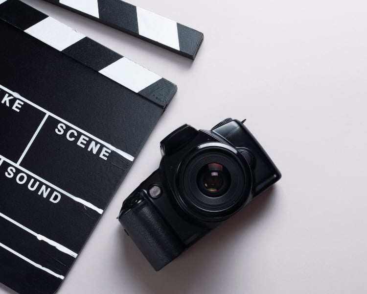 A black camera and a clapperboard lying side by side on a white surface.