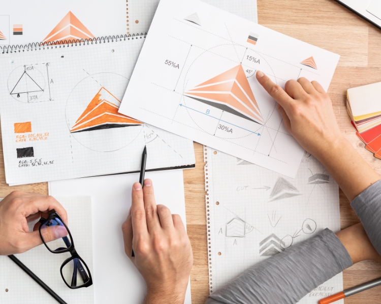 Two individuals are discussing the placement and angle of an orange logo design on a piece of paper.