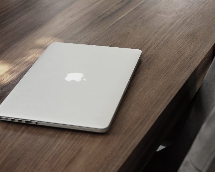 A closed silver laptop with apple brand placed over a wooden table.