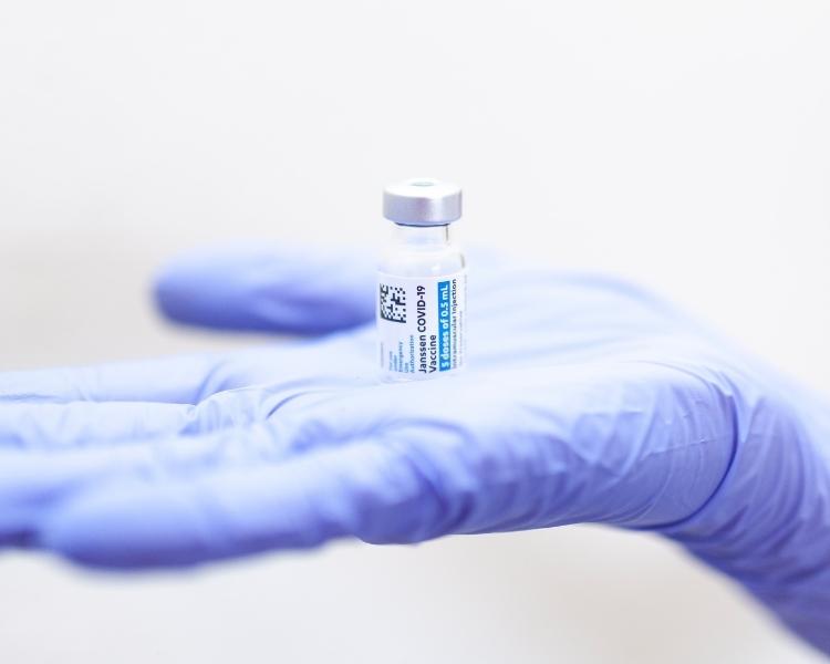 photo of a vaccine bottle as held by a medical personnel with blue gloves on