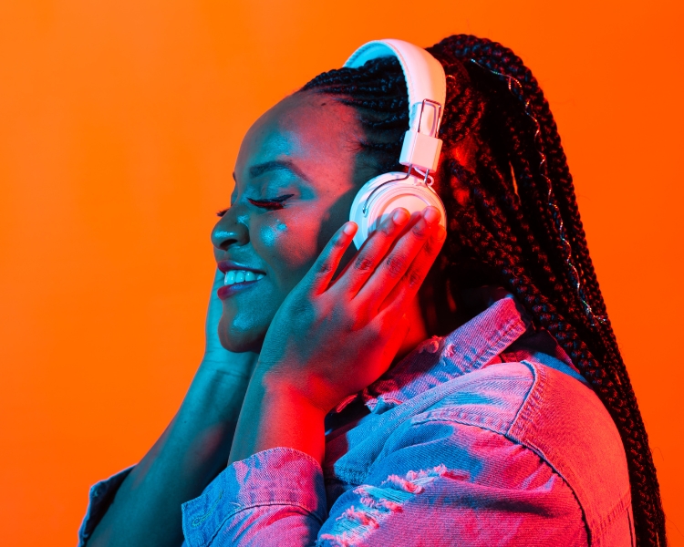 A woman feeling the music through her white headphone against an orange background.