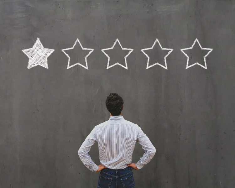 A man is observing a grey wall with a drawing of five stars, created using white chalk. Notably, only one star has been shaded.