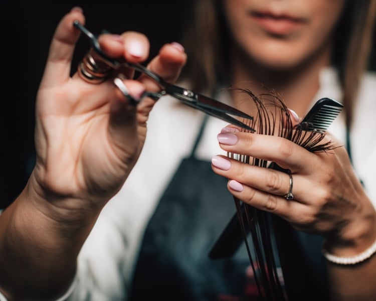 a woman hairstlist cutting or styling a hair with scissors and comb in her hands