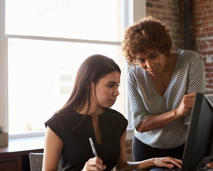 designer mentor looking at its student's work while she's working in front on her monitor and tablet