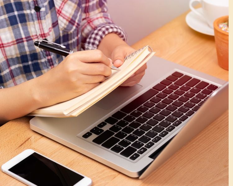 Hands on a notebook with laptop and black ballpen